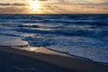 Picturesque colorful sunset over the Baltic Sea with glowing clouds and reflections on the small waves on the sandy beach. Royalty Free Stock Photo